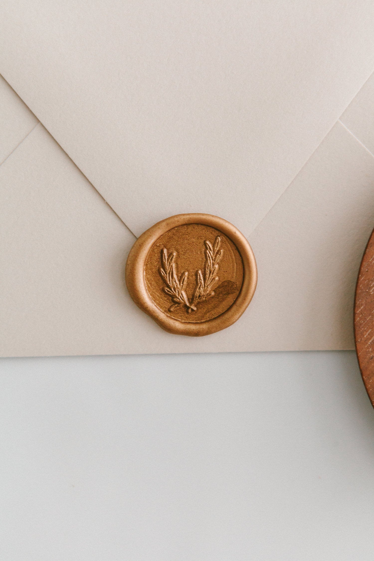 A close-up of a golden olive crest wax seal, styled on a beige sealed envelope on a white surface