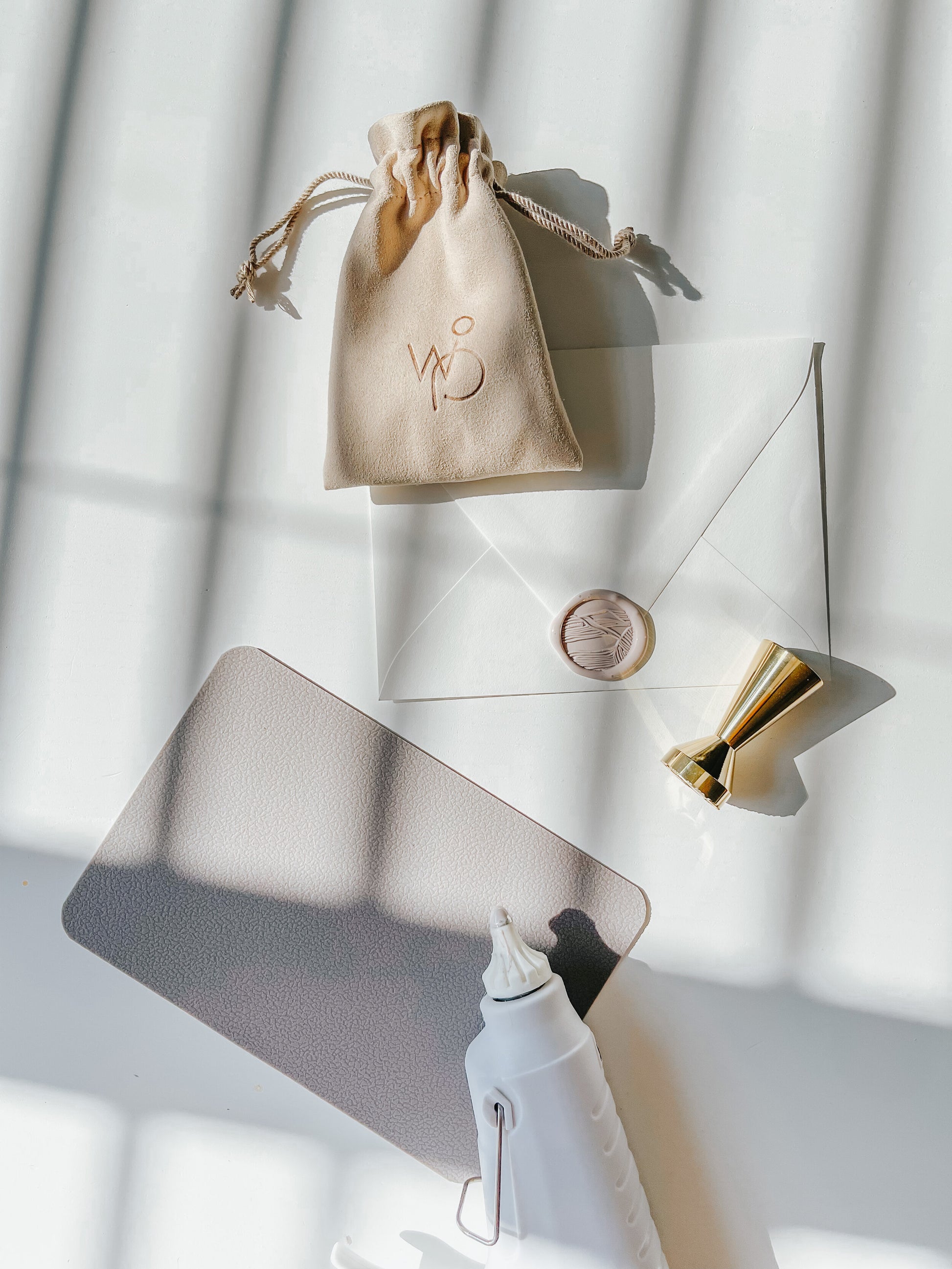 Wax sealing setup with a gold brass sand dunes wax stamp, envelope, suede pouch, and a white wax glue gun on a sunlit surface
