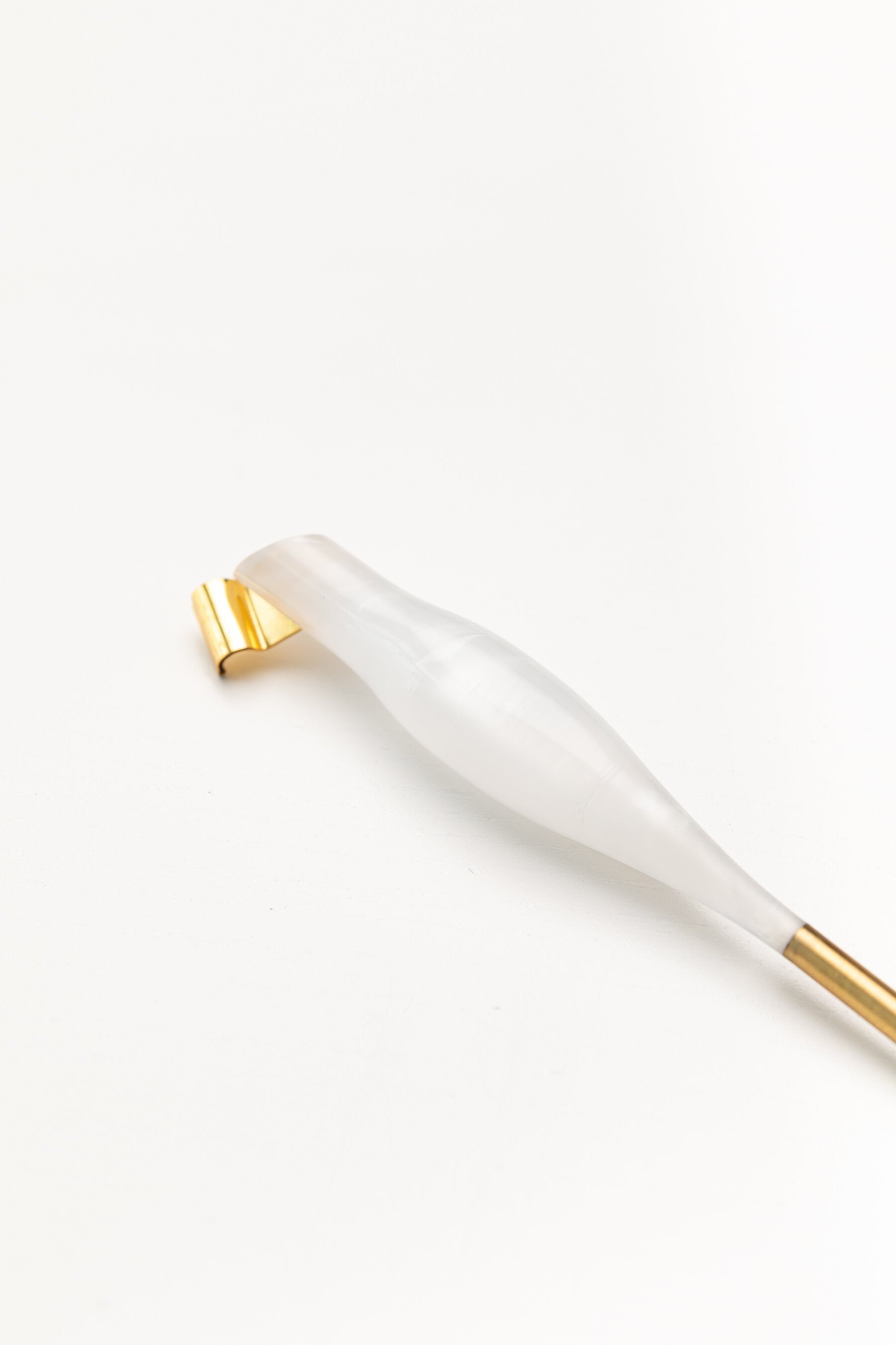 Close-up of a pearl-toned oblique calligraphy pen with a sleek design and a gold brass flange, placed on a white background