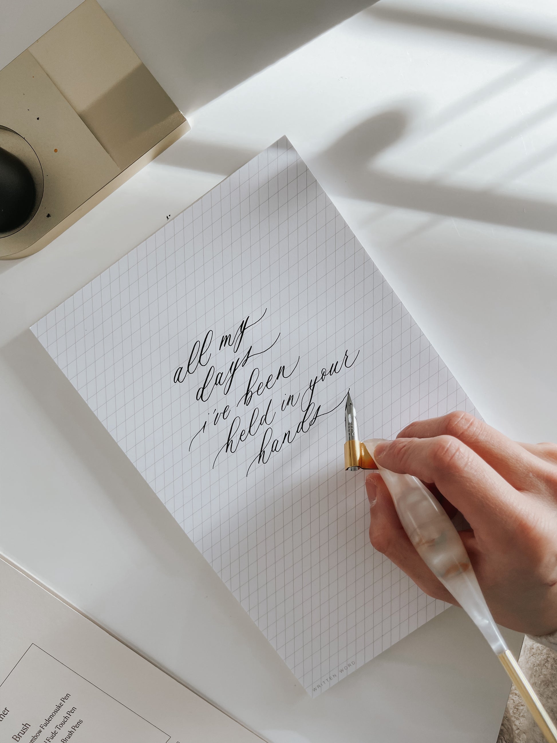 Hand holding a resin calligraphy pen writing on slanted grid notepad with beautiful calligraphy