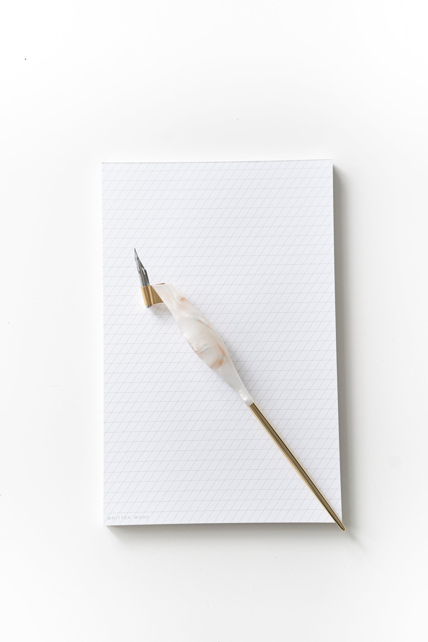 Calligraphy pen resting on a slanted grid notepad, ready for practice with ink-friendly sheets