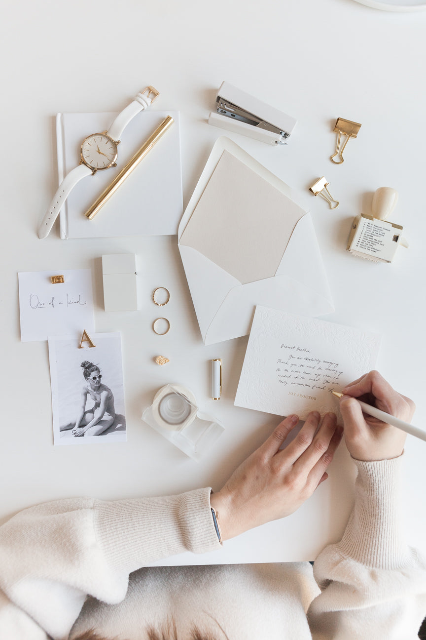 Minimal stationery flat lay with embossed card, envelope, and gold office accessories