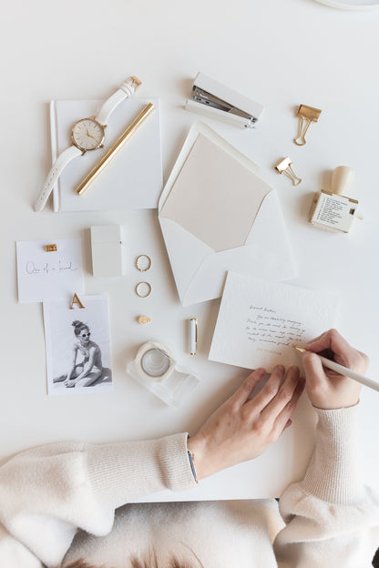 Minimal stationery flat lay with embossed card, envelope, and gold office accessories
